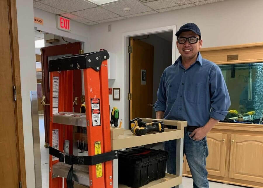 Maintenance worker Generoso Gozo poses by a cart carrying power tools and a ladder