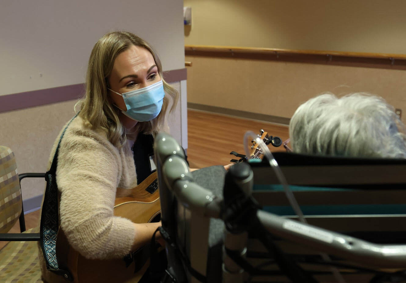 Nadine Verboa plays music on her guitar to a resident who is sitting in a wheelchair