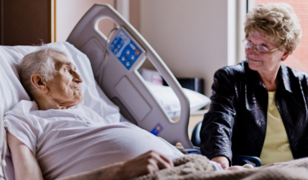 A palliative patient in a hospital bed with his wife by his side.
