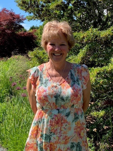 Smiling woman in summer dress poses in front of trees and vegetation