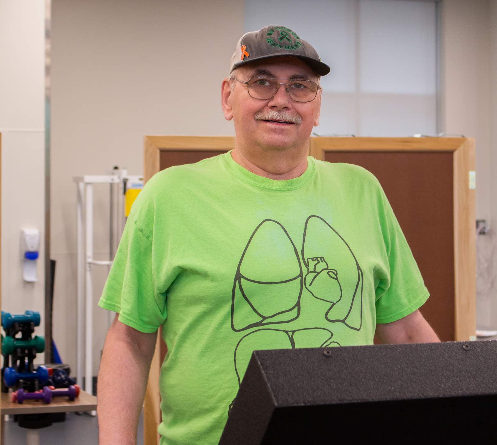 Senior man stands on a treadmill in front of dumbbells