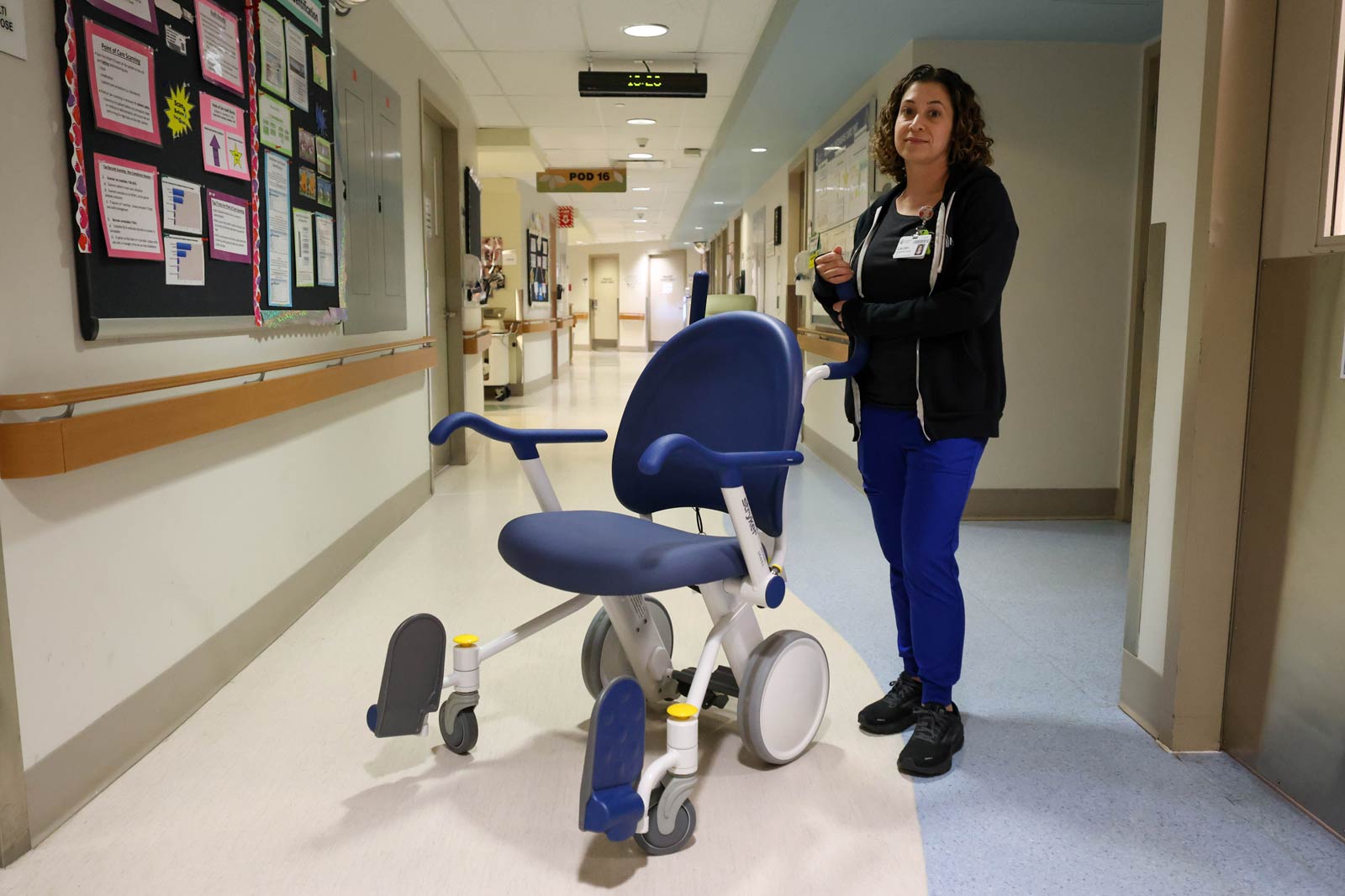 Woman wearing Covenant Health name tag standing next to a transfer chair in a hospital hallway