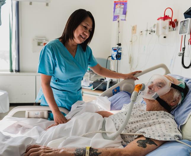 Staff member interacts with a patient in a hospital bed.