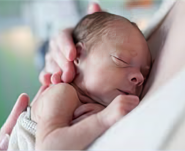 A newborn baby naps against a parent's chest.