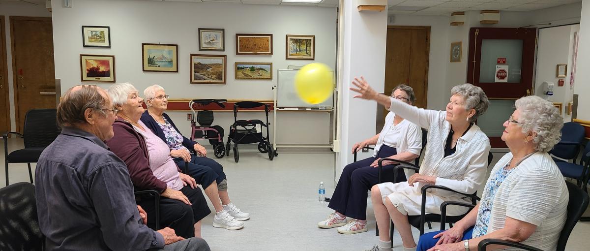 Seniors sitting together while keeping a balloon in the air.