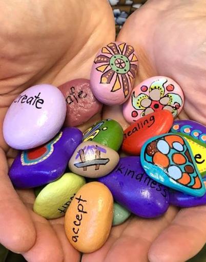 Hands cradling rocks painted with images and words such as create, healing, kindness, and accept