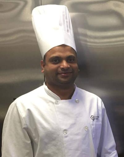 Joseph Vellam in a Covenant Health chef uniform posing in front of stainless steel fridges