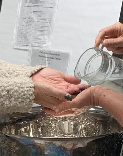 A pitcher of water about to be poured on open palms over a metal basin