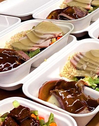 Rows of food trays containing rice turkey with gravy and vegetables on a table
