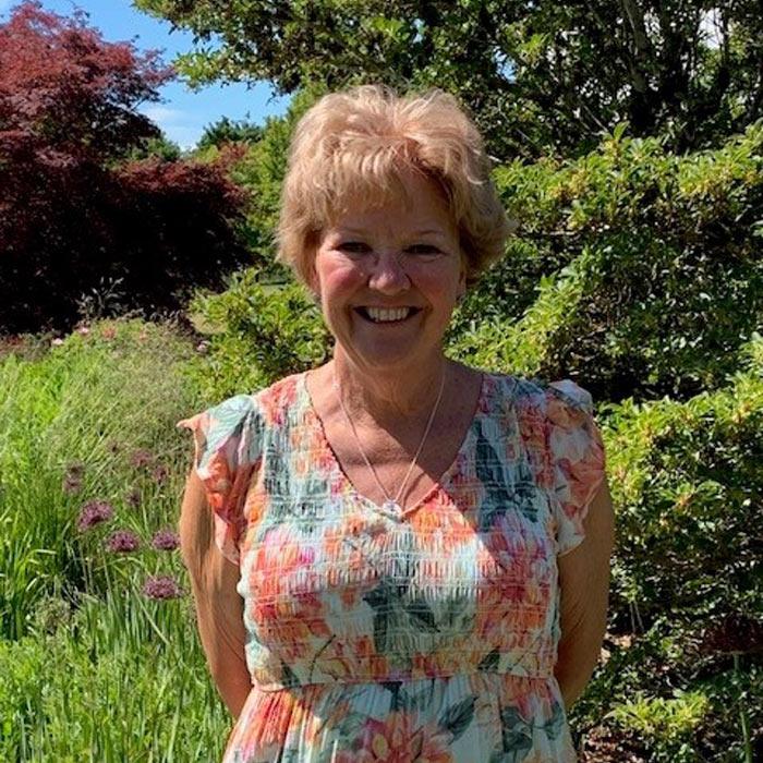 Smiling woman in summer dress poses in front of trees and vegetation