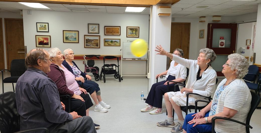 Seniors sitting together while keeping a balloon in the air.