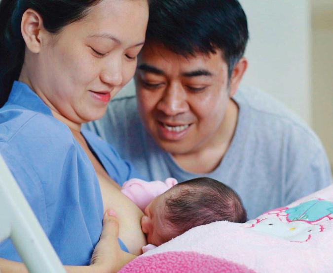 A mother breastfeeds her newborn with her partner at her side.