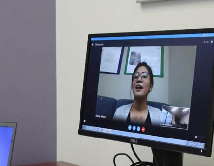A woman displayed on a computer monitor speaks during a virtual meeting