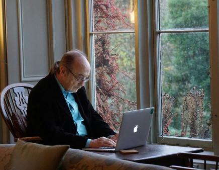 A senior works on a laptop at a dining table.